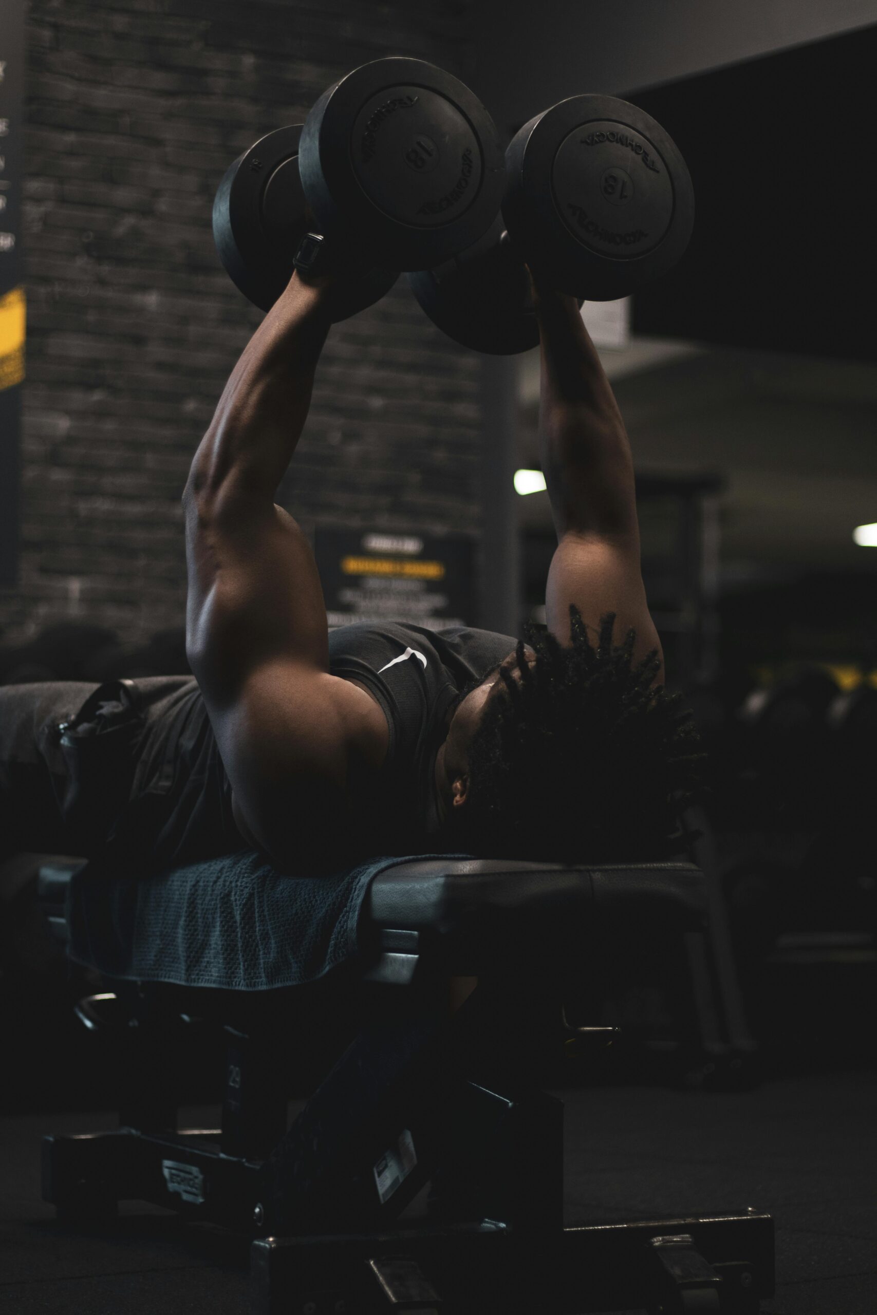 An African American man focused on a dumbbell press in a gym setting.