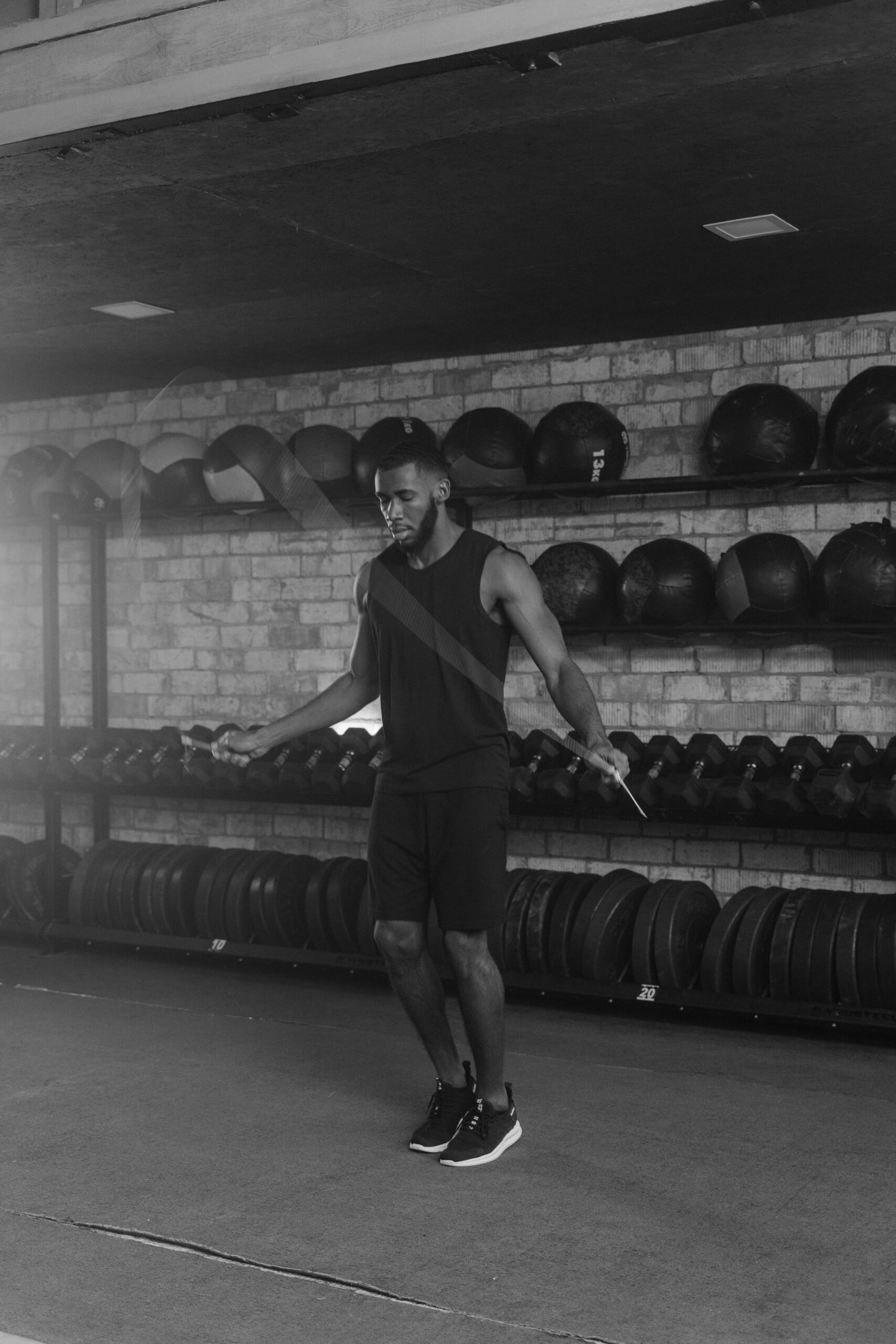 Athletic man jumps rope in a monochrome gym setting, emphasizing fitness and strength.