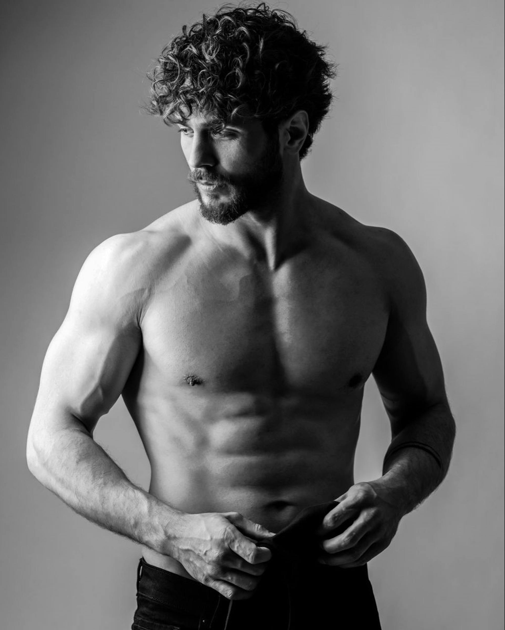 Black and white portrait of a muscular man with curly hair and beard, showcasing strength.